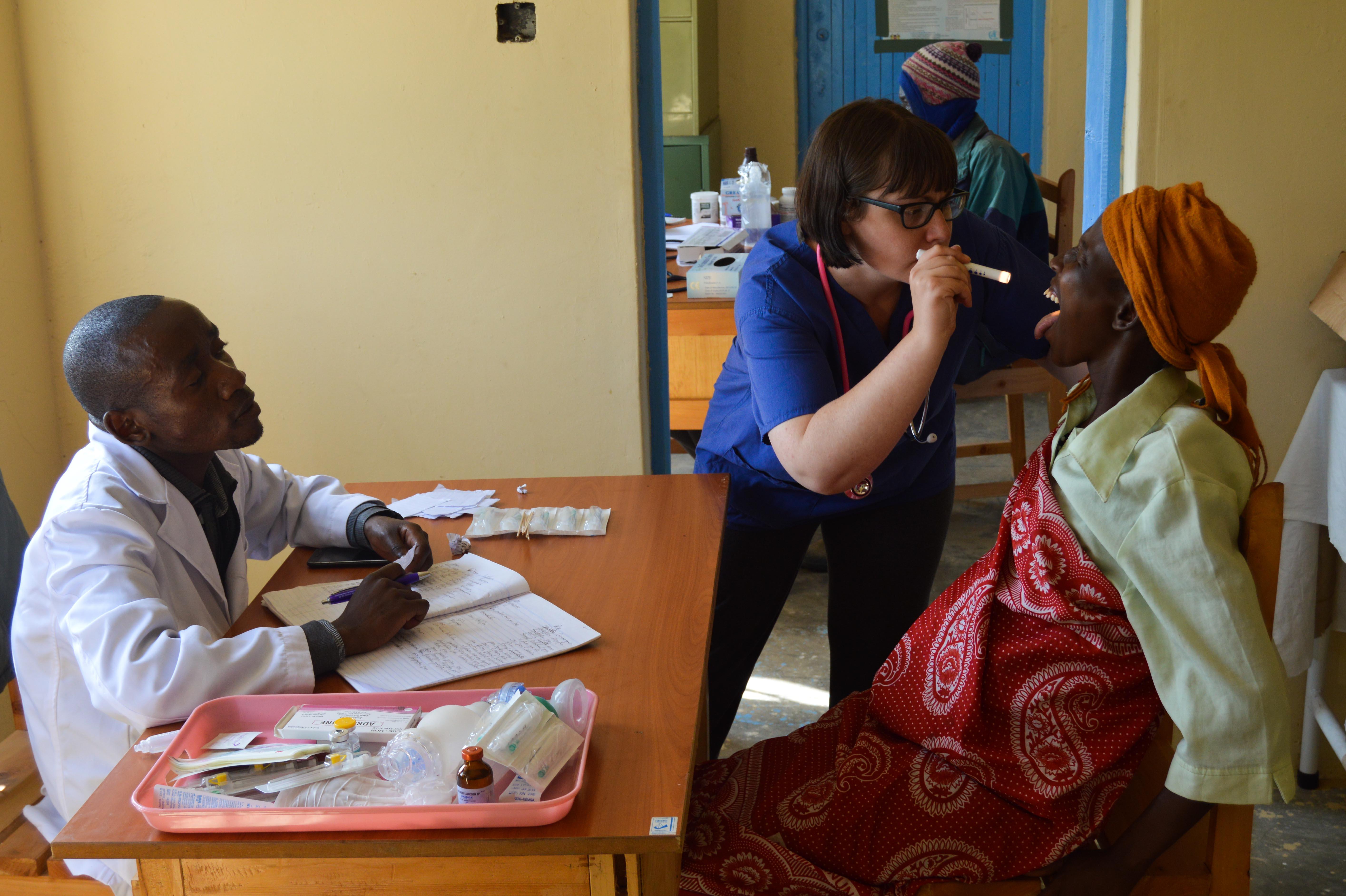 Female Projects Abroad intern examines a woman's mouth with a pen torch during an outreach as part of her medical work experience placement in Kenya. Female medical intern examines a woman's mouth with a healthcare worker at a medical outreach in Kenya.